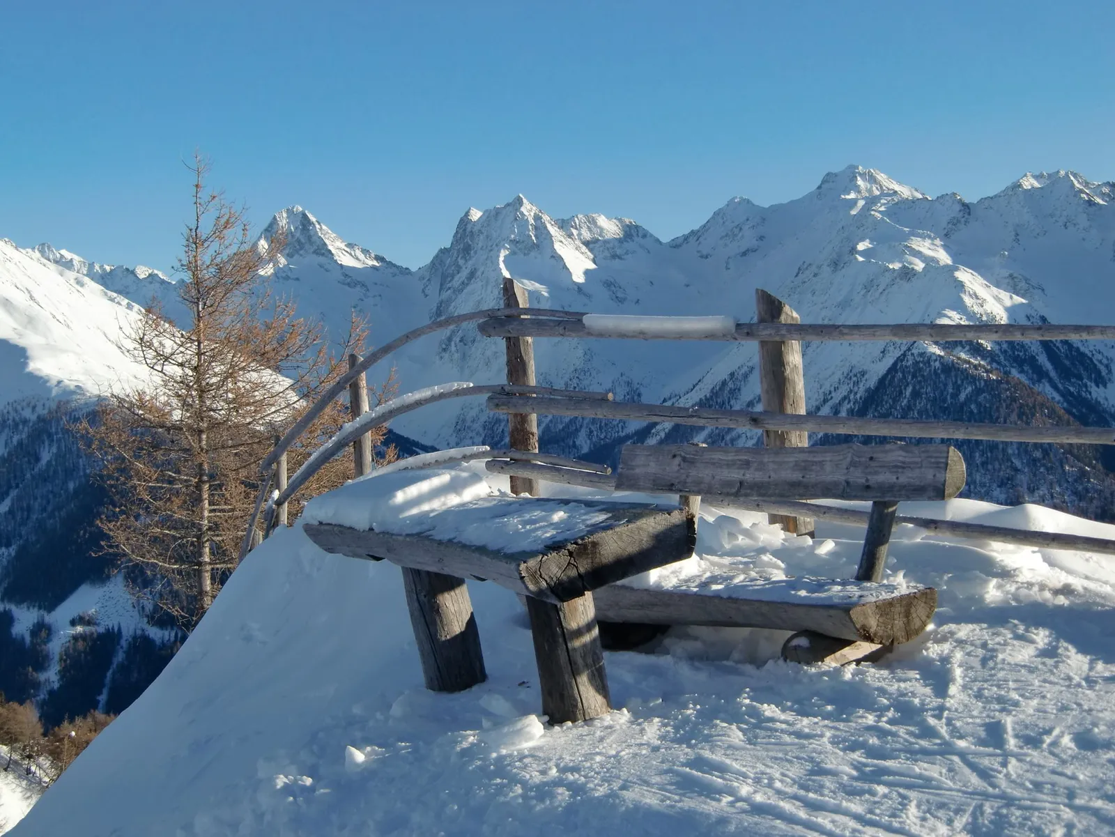 Verschneite Holzbank vor den Gipfeln der Hohen Tauern